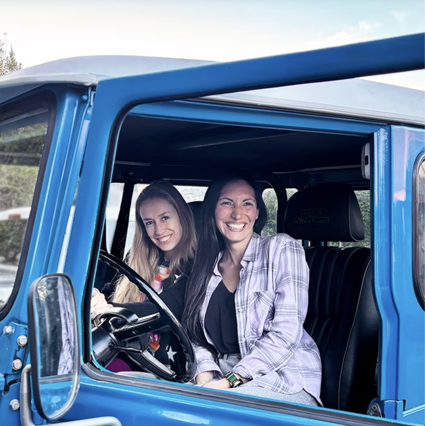 Dos mujeres sonriendo dentro de un Jeep clásico azul